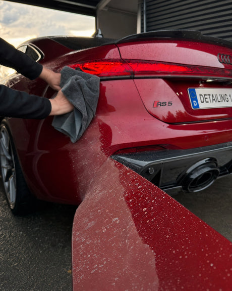 Daniel poliert mit dem Mikrofasertuch das Heck eines roten Audi RS 5; eine Zone glänzt schon tief und perlt, daneben noch mat