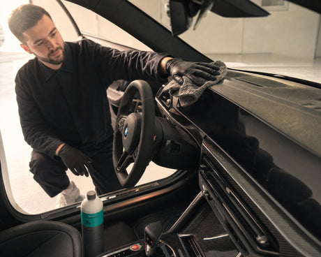 Daniel wischt in der Pollensaison den gelben Pollenfilm vom Armaturenbrett eines weißen BMW M2 — gezeigt im Artikel „Auto-Innenraum in der Pollensaison reinigen: Cockpit, Lüftung, Filter“