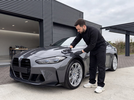 Daniel poliert die Motorhaube eines dunklen Sportwagens mit silbernen Felgen unter weichem bewölkten Tageslicht — gezeigt im Artikel „Heute bedeckt, ab morgen Sonne. Dazwischen liegt dein Polier-Tag."